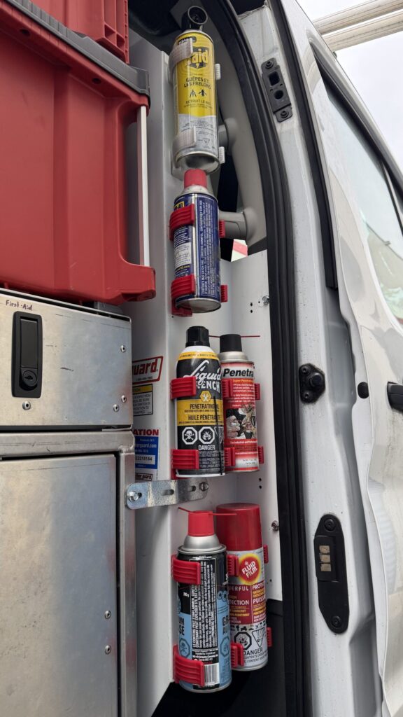 Multiple aerosol spray cans secured in red 3D printed holders mounted on the vertical panel inside a work van.