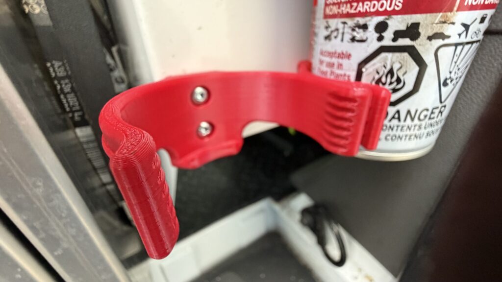 Front angle view of a bright red 3D printed aerosol spray can holder mounted on a white surface inside a work van.