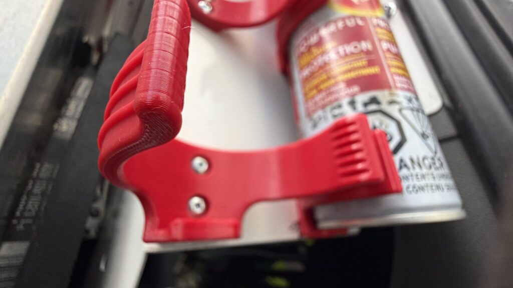 Close-up of a red 3D printed aerosol spray can holder mounted in a work van.