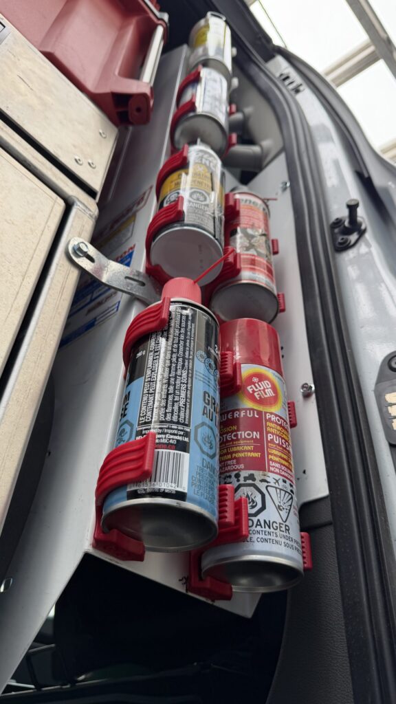 A close-up view of 3D printed red holders securing multiple aerosol spray cans in a work van.