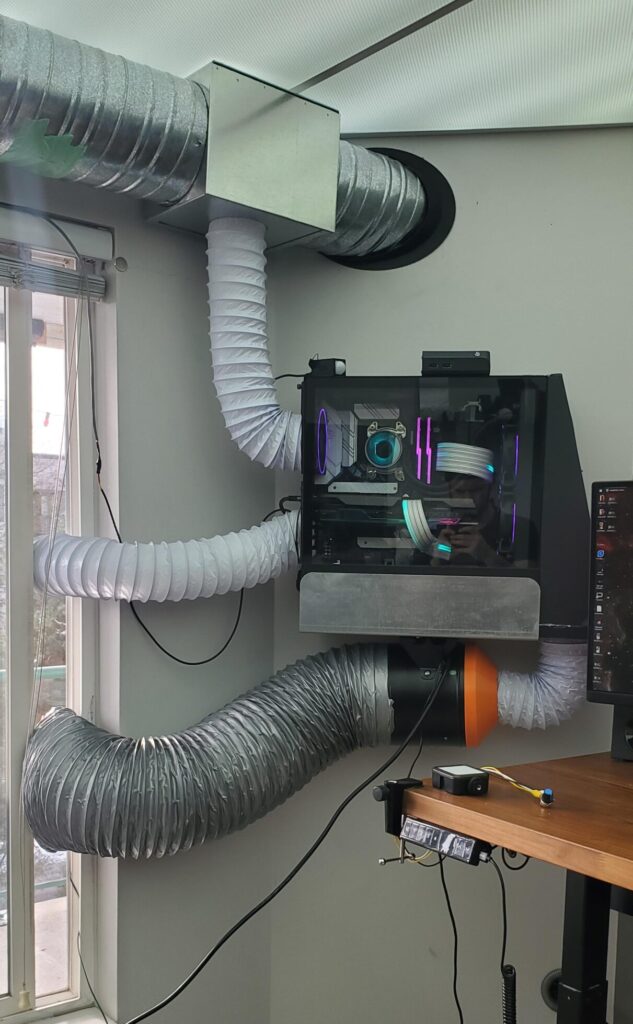A gaming computer mounted on a wall with flexible air conditioning ducts attached for ventilation and cooling.
