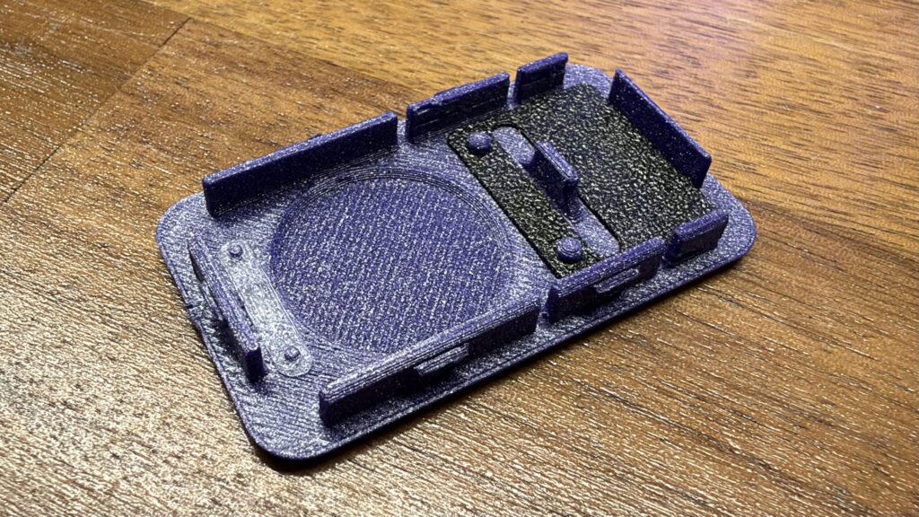 A purple 3D printed keyfob housing with integrated button piece and retaining clips rests on a wooden surface.