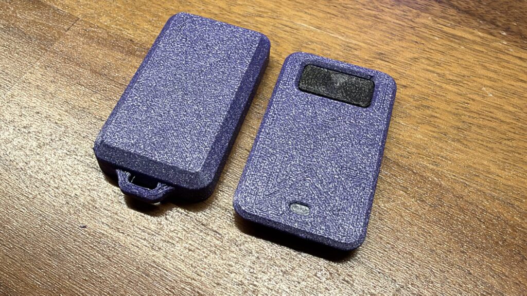 Two textured purple 3D-printed keyfob housings resting side by side on a wooden surface.