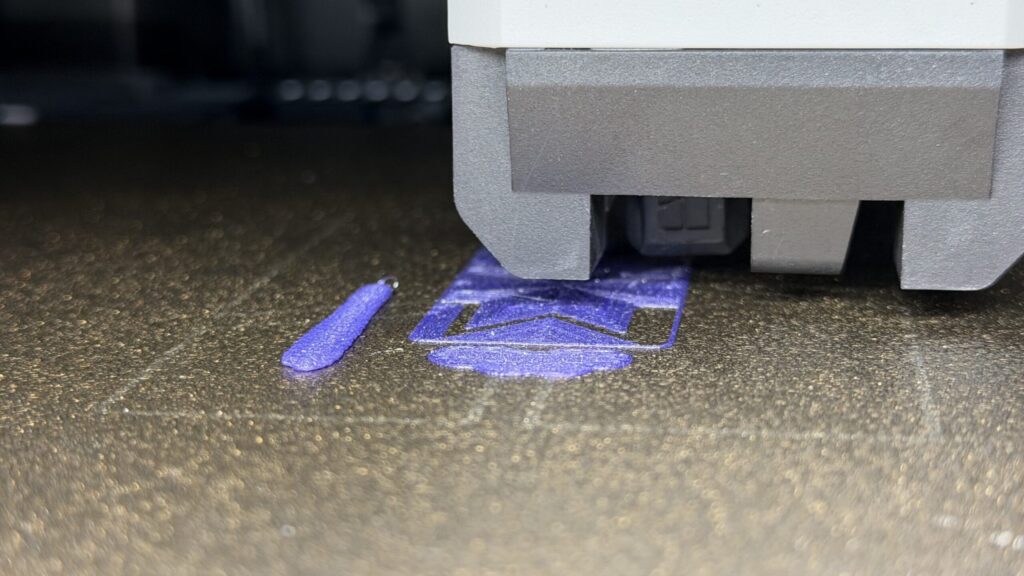 A 3D printer nozzle extrudes purple filament onto a textured print bed to create a garage door remote.