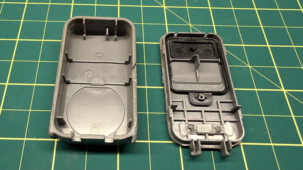 Two halves of a grey keyfob housing lying open on a green cutting mat.